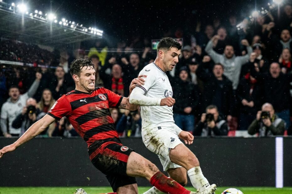 Jogadores disputam a bola de forma intensa durante partida de futebol em estádio lotado