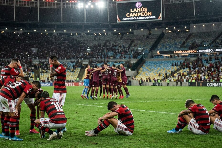 Jogadores do Flamengo desolados no gramado do Maracanã enquanto atletas do Lanús celebram ao fundo