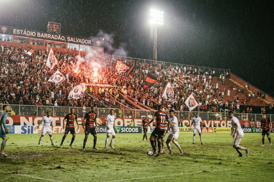 Jogadores em campo no estádio Barradão durante partida noturna de futebol