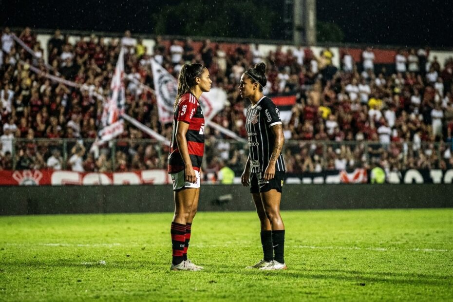 Jogadoras de futebol feminino perfiladas no gramado de um estádio à noite representando a rivalidade de um clássico